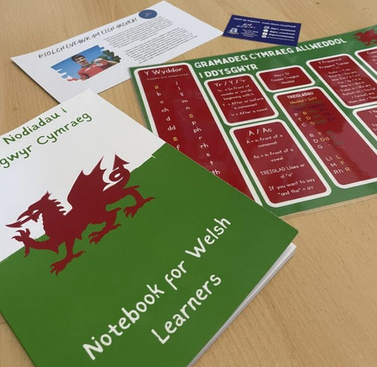 Welsh-language learning notebooks arranged together, featuring colourful bilingual designs.