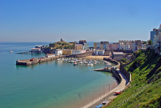Colourful houses overlooking Tenby Harbour in Pembrokeshire, with boats moored in the harbour, sandy beach, stone harbour walls, and the ruins of Tenby Castle on Castle Hill above the sea.