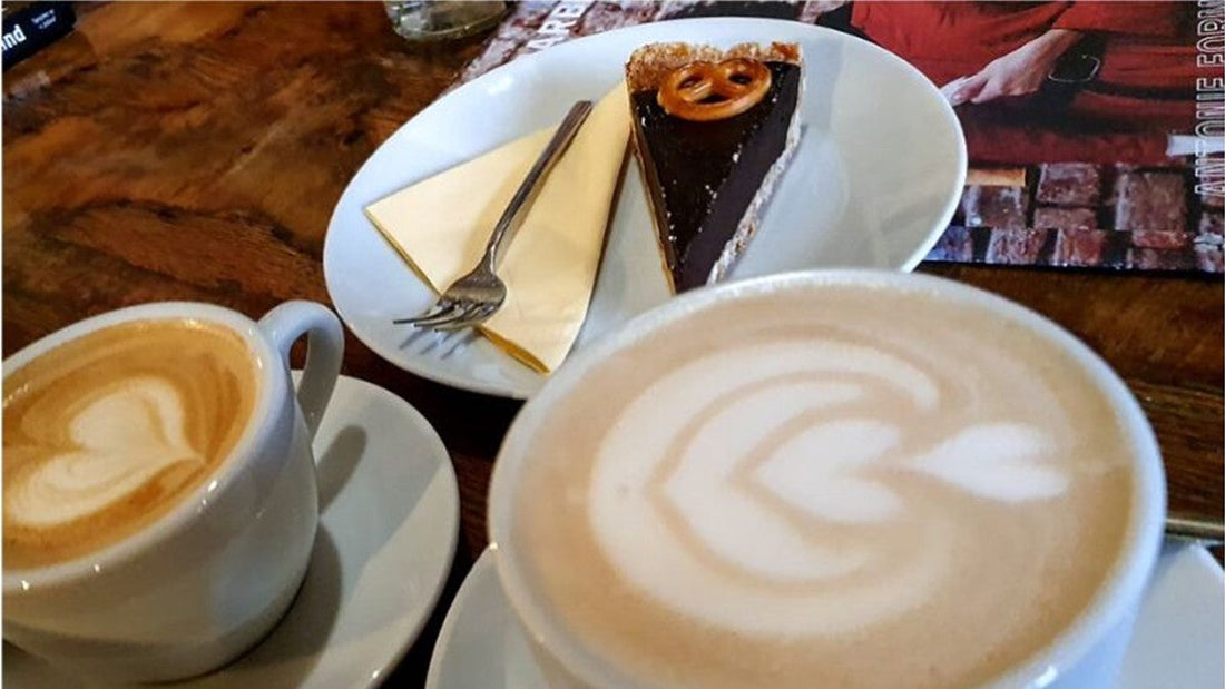 Two cups of coffee with latte art beside a slice of chocolate cake