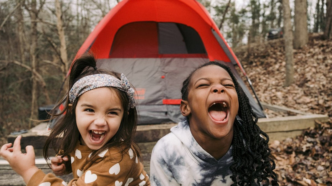 Two children laughing beside a red camping tent