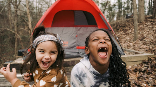 Two children laughing beside a red camping tent