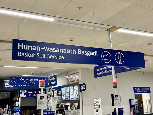 Bilingual Welsh and English directional signs inside a supermarket in Wales