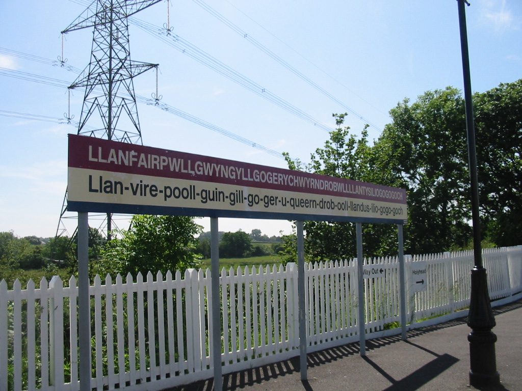 Railway station sign at Llanfairpwll showing the long Welsh place name and an English-speaker pronunciation guide