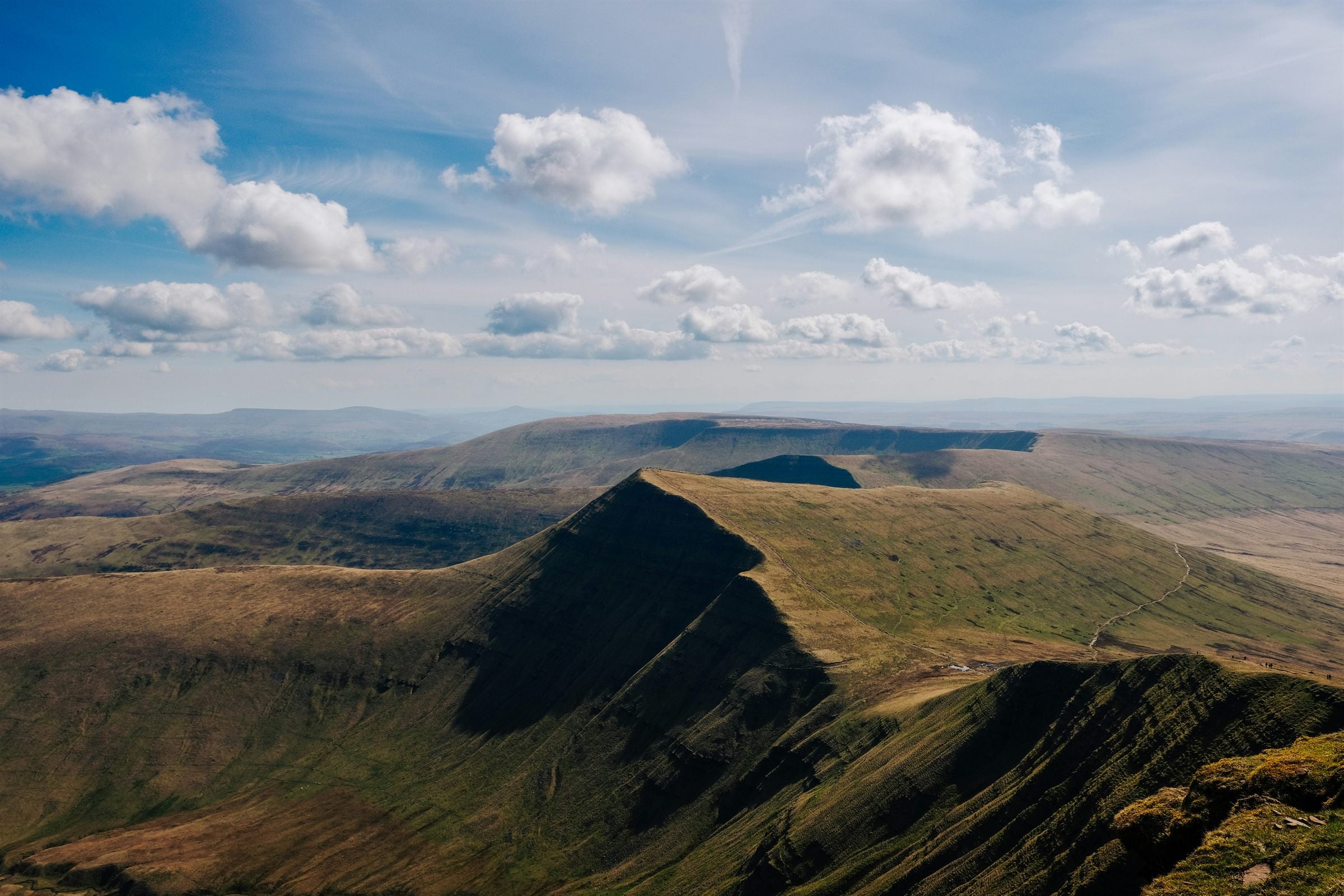 Panoramic view across Pen y Fan and the surrounding Bannau Brycheiniog mountain ridges beneath a bright, cloud-filled sky.